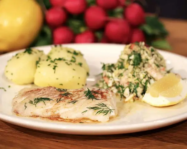 En tallrik med stekt kolja, dill, potatis och en citronskiva. Ett perfekt kolja recept för en god middag.