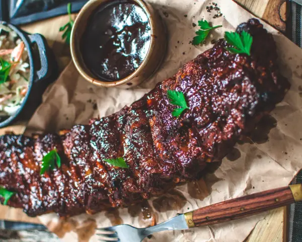 Saftiga spareribs i ugn, glaserade och serverade med en skål coleslaw och BBQ-sås. Perfekt för en festmåltid!