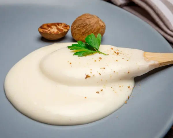 Krämig bechamelsås på en tallrik med muskotnötter och persilja. Ett perfekt bechamelsås recept för alla tillfällen.