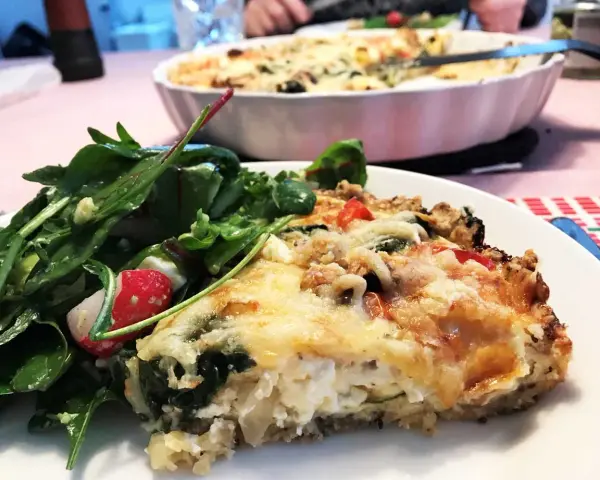 En bit krämig vegetarisk paj med ost och grönsaker, serverad med en fräsch sallad.