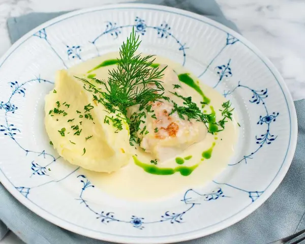 En vacker tallrik med torskrygg recept, serverad med krämigt potatismos och en grön dillolja.