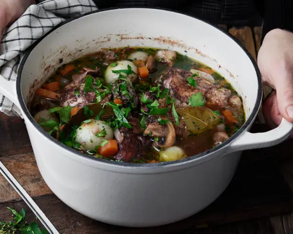 En gryta med mustig coq au vin, fylld med möra kycklingbitar, champinjoner, lök och morötter, toppad med färsk persilja.