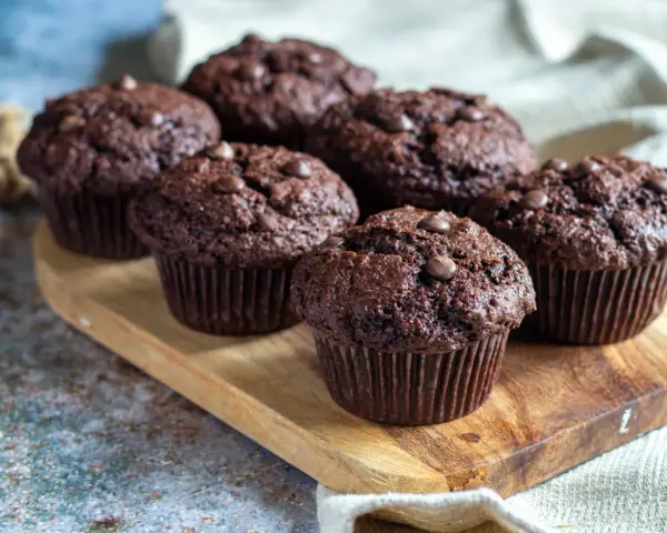 Fem saftiga chokladmuffins med chokladknappar på en träbricka. Perfekt för ett chokladmuffins recept.