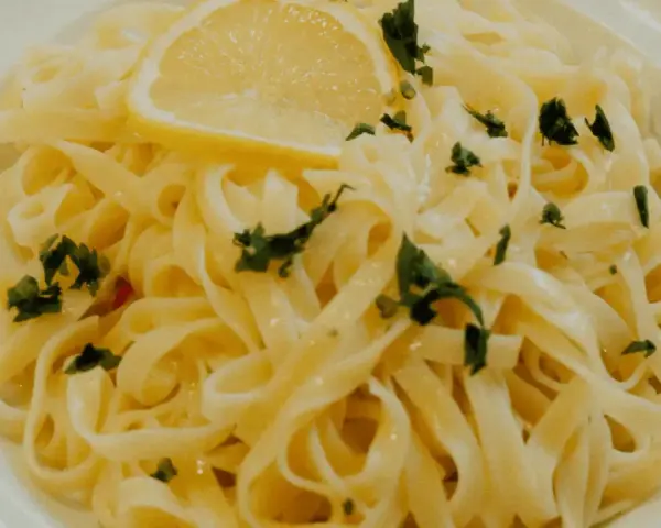 En portion krämig citronpasta med färsk persilja och en citronskiva. Perfekt till ett glas vitt vin.