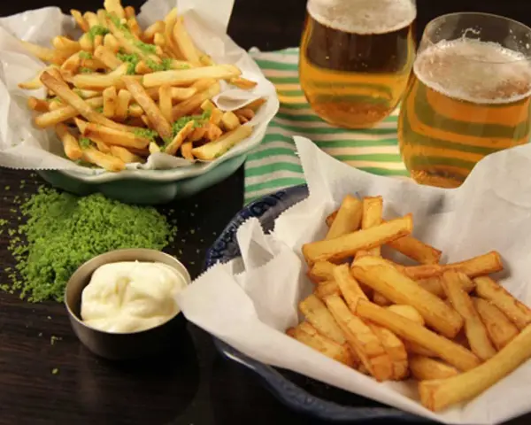 Två skålar med krispiga pommes frites, en med grön kryddning, bredvid två glas öl och en skål majonnäs.
