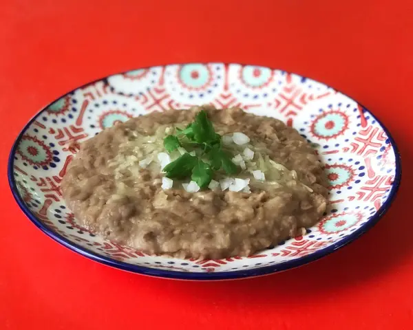 En tallrik med refried beans, toppad med lök och persilja. Ett enkelt och gott refried beans recept.