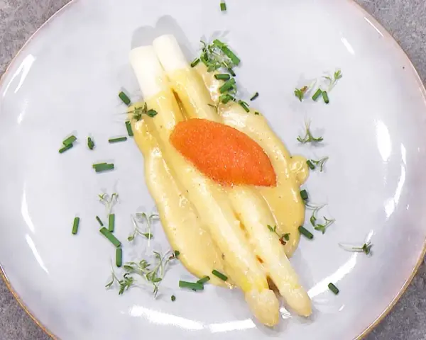 Vit sparris med krämig hollandaisesås, toppad med rom och garnerad med gräslök och örter. En klassisk och elegant rätt.