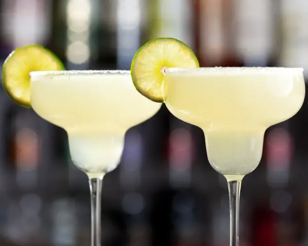 Två frostiga frozen margaritas med saltkant och lime, redo att avnjutas.