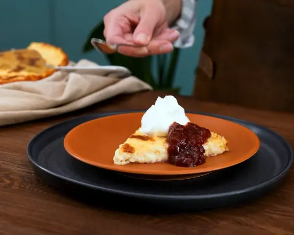 En bit krämig ostkaka med sylt och grädde, redo att avnjutas. Ett perfekt ostkaka recept för fikat.