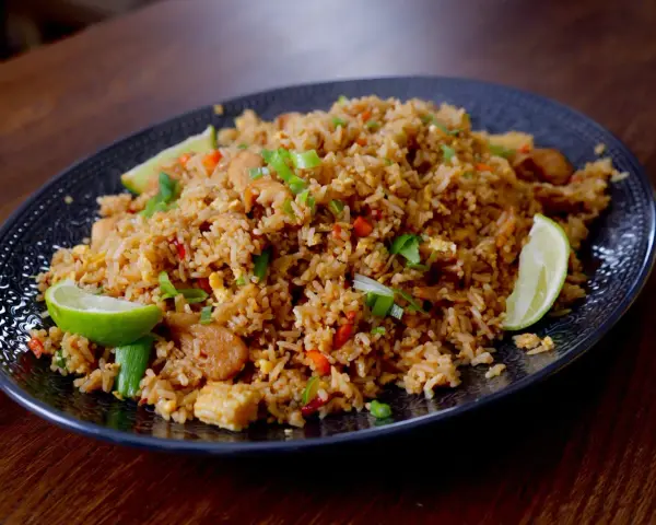 En tallrik med utsökt fried rice, garnerad med limeklyftor och salladslök.