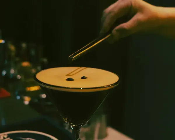 En hand lägger kaffebönor på en krämig espresso martini.