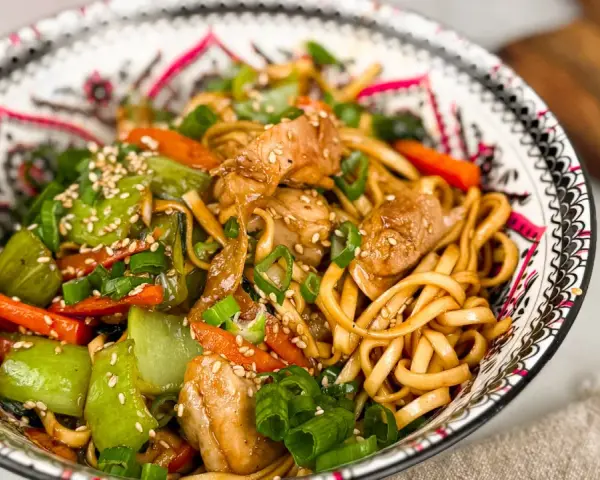 En skål med kycklingwok med nudlar, grönsaker och sesamfrön. En härlig och färgstark måltid.