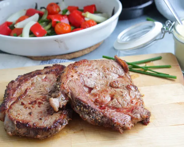 Två saftiga entrecôte-biffar på skärbräda, redo för ett utsökt entrecote recept. Grönsaker i bakgrunden.
