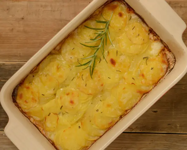 En ugnsform med gyllene, tunna potatisskivor, en klassisk pommes anna, toppad med en rosmarinkvist.