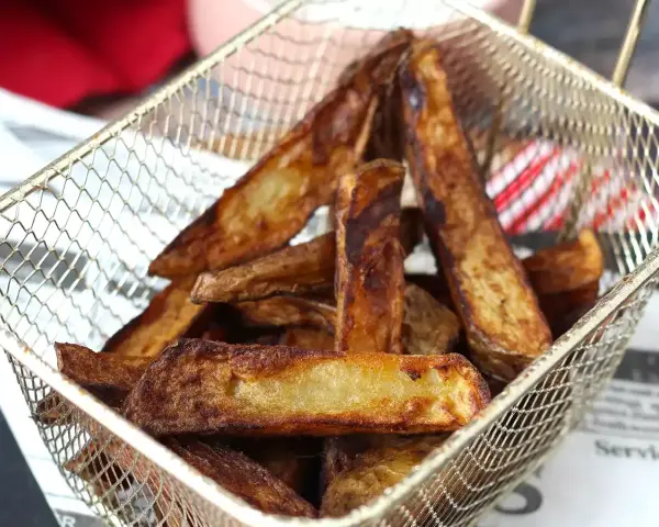Krispiga pommes frites i airfryer, gyllene och redo att serveras i en metallkorg.