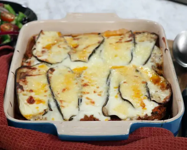 En ugnsform med en gyllene, bubblande moussaka, redo att serveras. Perfekt för ett mysigt middagsrecept.