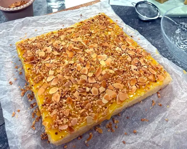En fyrkantig silviakaka med gul glasyr och strössel av hackade nötter och mandel. Perfekt för ett fika-recept!