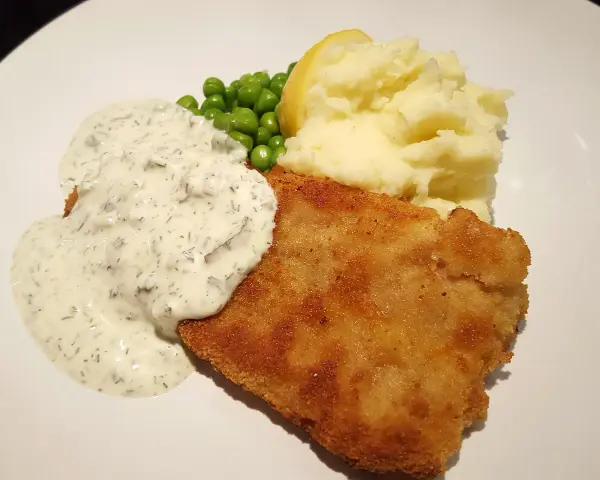 En gyllene panerad fisk med krämig sås, ärtor och potatismos. En klassisk och god måltid.