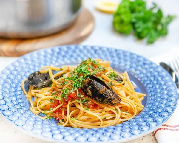 En tallrik med frutti di mare pasta, toppad med färsk persilja och serverad i en blåmönstrad skål.