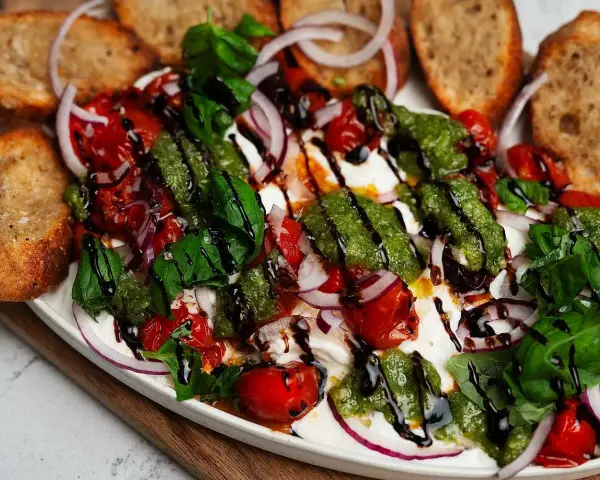 En krämig burrata med tomater, rödlök, basilika och pesto. Perfekt tillbehör till grillat bröd. Ett enkelt burrata recept.