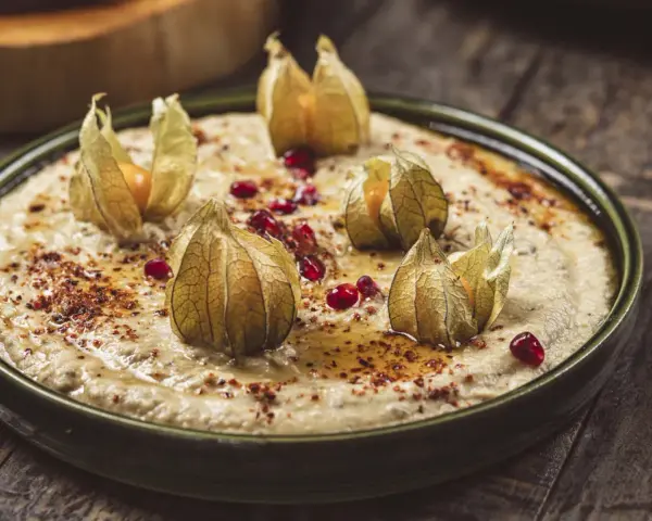 Krämig baba ganoush toppad med physalis och granatäppelkärnor på en rustik träyta.