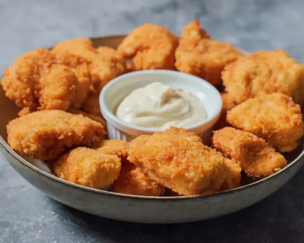 En skål med gyllene, krispiga chicken nuggets och en liten skål med krämig dipp. Perfekt för en snabb och god måltid.
