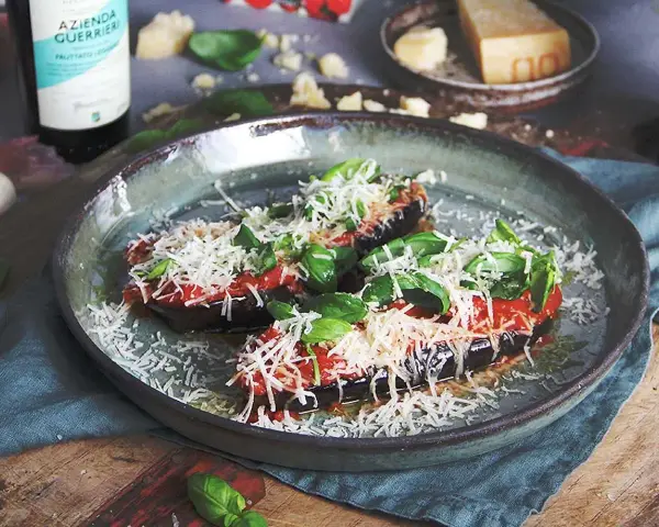 Halverade auberginer toppade med tomatsås, basilika och riven ost, redo att tillagas i ugnen. En härlig aubergine i ugn.