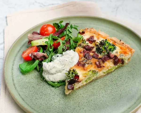 En bit ost och broccolipaj med knaperstekt bacon, serverad med en fräsch sallad och en klick vitlökssås.