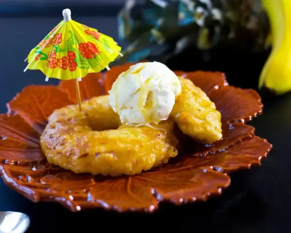 Friterad banan med vaniljglass och en liten gul parasoll. En tropisk dessert som smakar sommar.
