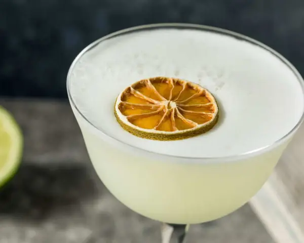 En krämig gin sour med ett skumtäcke och en torkad lime som dekoration.