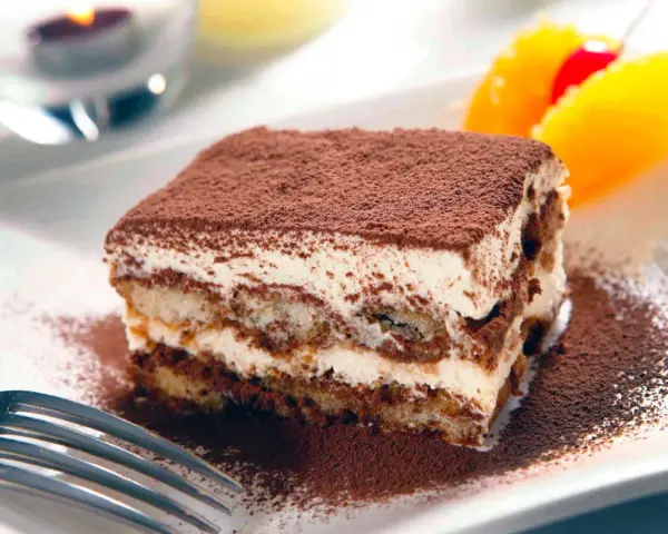 En bit krämig tiramisu, pudrad med kakao, serveras med frukt. Perfekt dryck till tiramisu.