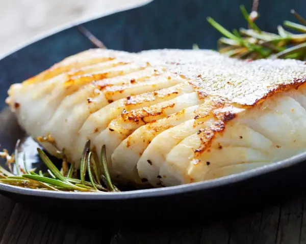 En saftig bit fryst torsk i ugn, gyllene och perfekt tillagad, med rosmarin i en mörk panna.