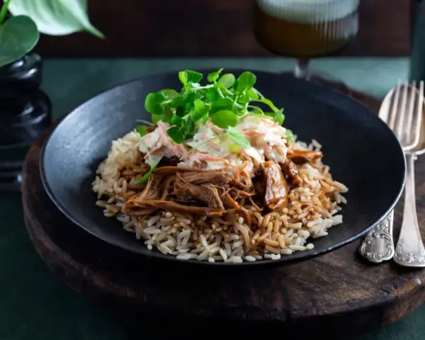 En tallrik med pulled pork med ris, toppad med krispig coleslaw och gröna blad. En härlig måltid som ser utsökt ut.