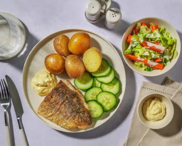 En tallrik med stekt vit fisk, kokt potatis, gurka och en klick majonnäs. Ett perfekt vit fisk recept för en snabb middag.