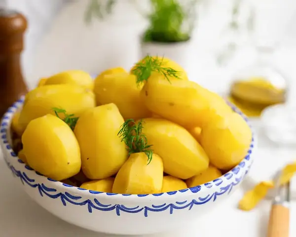 Nyskållade, gula potatisar i en blåvit skål, redo att koka. Dillkvistar ger en fräsch touch.