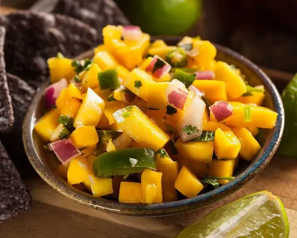 En skål med färgglad mango salsa, med tärnad mango, rödlök, grön paprika och koriander. Serveras med tortillachips och limeklyftor.