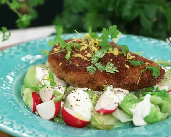 En gyllene kyckling kiev toppas med citronzest och persilja, serverad på en bädd av krispig sallad med rädisor och krämig dressing.