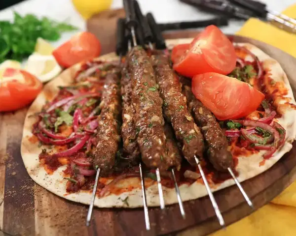 Grillade Adana kebabspett på en bädd av tunnbröd med rödlök, tomat och persilja. Ett perfekt adana kebab recept för en smakrik måltid.