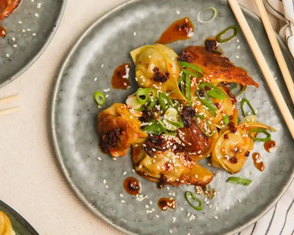 Stekta dumplings med en kryddig sås, toppade med sesamfrön och salladslök. En utsökt dumplings sås som gör rätten komplett.