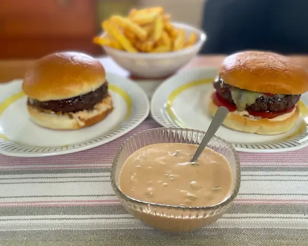 Två hamburgare med pommes frites och en skål med hemlagad hamburgerdressing. Perfekt för en mysig hemmakväll!