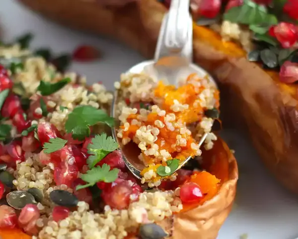 En sked tar en portion av ett läckert quinoa recept fyllt med pumpa, granatäpple och örter, serverat i en ugnsbakad butternut squash.