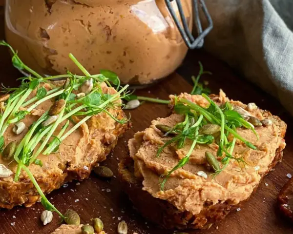 Två rostade brödskivor med krämigt refried beans, toppade med groddar och frön. En burk med pålägget syns i bakgrunden.