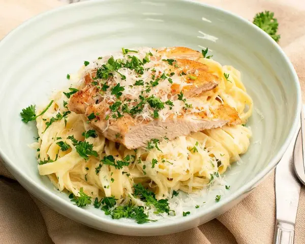 En krämig portion chicken alfredo med tagliatelle, toppad med grillad kyckling, parmesan och färsk persilja.