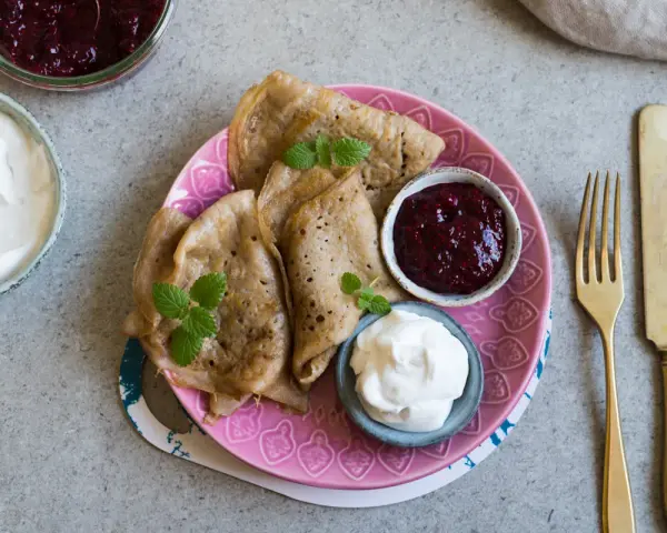 En tallrik med glutenfria pannkakor, serverade med sylt och grädde. En härlig frukost eller fika!