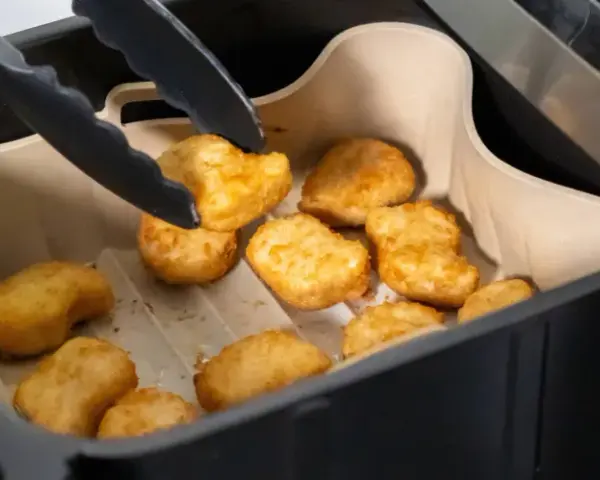 Tång tar upp gyllene, krispiga tater tots ur en airfryer.