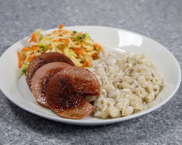 En tallrik med stuvade makaroner, stekt falukorv och en sallad på vitkål och morötter.