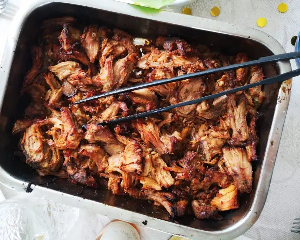 Saftigt, långkokt fläskkött i en ugnsform, perfekt för ett carnitas recept. Tång ligger redo att servera.