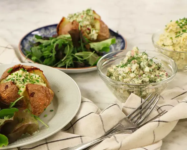 Två bakade potatisar med en krämig bakad potatis fyllning, serverade med en fräsch sallad och två skålar med olika röror.