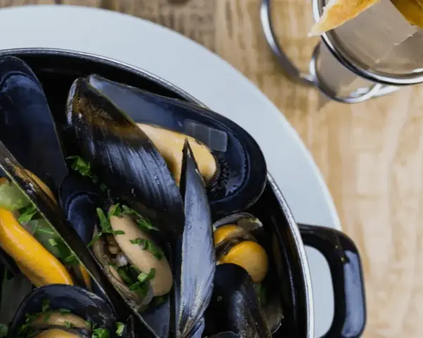 En stor kastrull med ångande blåmusslor, perfekt för en måltid med vin till moules frites. Pommes frites syns i bakgrunden.