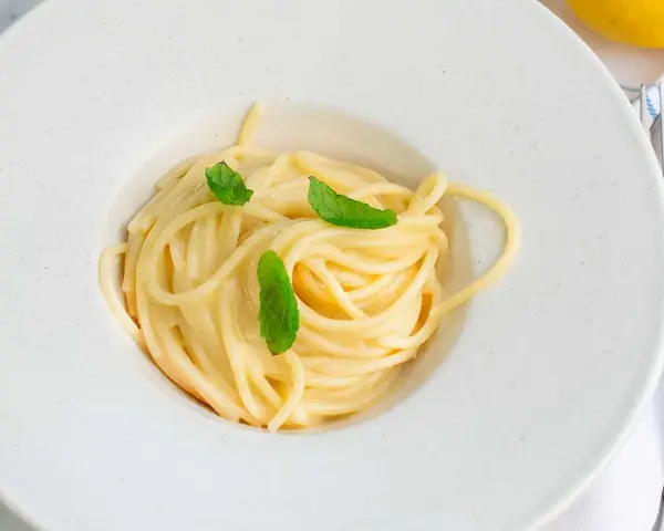 En krämig pasta limone, serverad i en vit skål med färska myntablad.